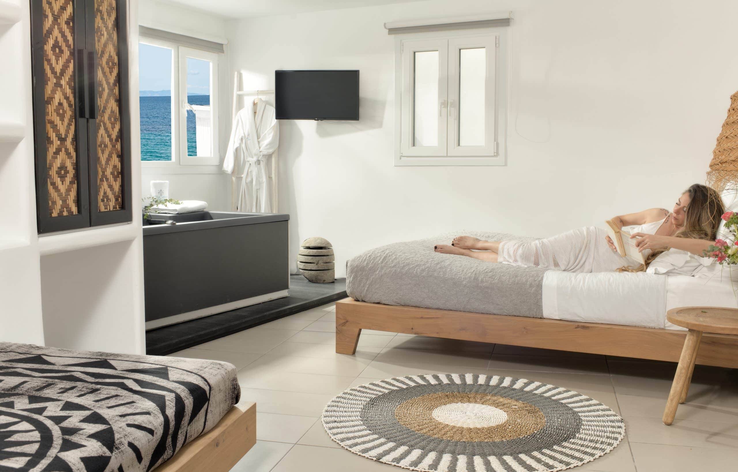 Guest relaxing on the bed of a bright suite with an indoor hot tub and a sea-view window